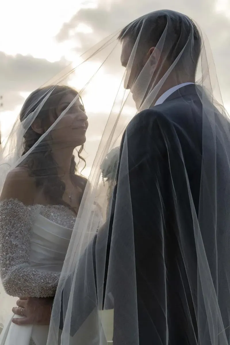 Les mariés face à face sous le voile de la mariée, au coucher du soleil
